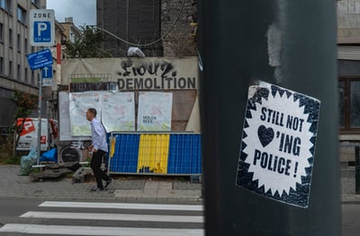 “仍然不爱”警察贴纸印在杆子上，可以俯瞰白天站在人行道旁的人